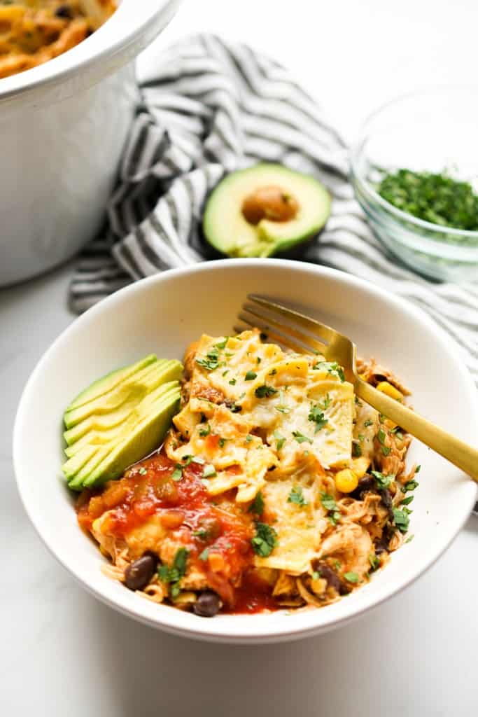 A bowl of chicken enchilada casserole topped with avocado and salsa