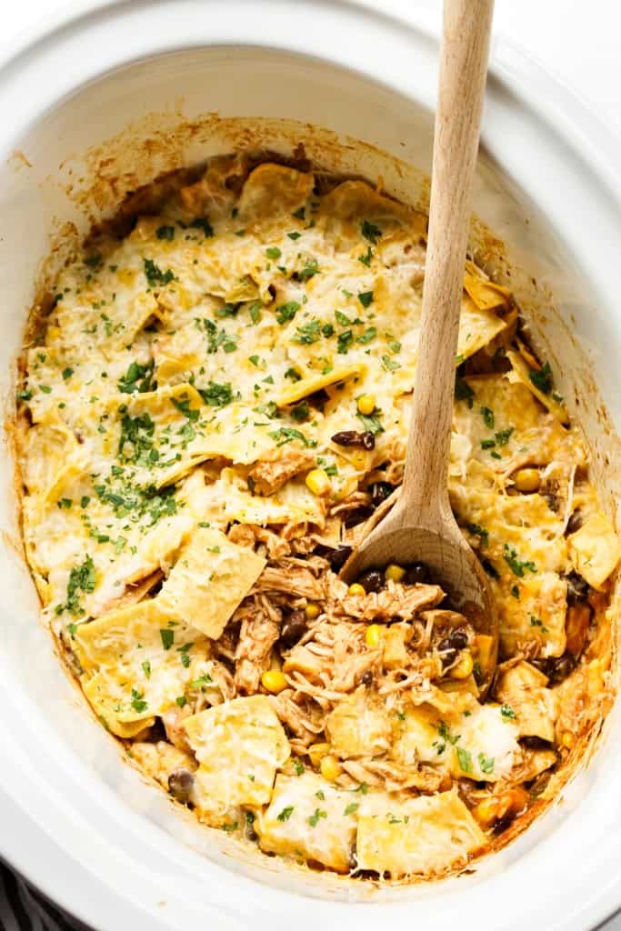 Chicken enchilada casserole in a crockpot, a wooden spoon digging into it