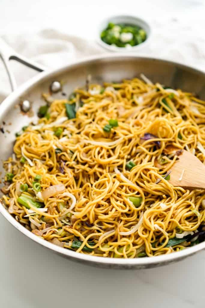 A large stainless steel skillet with chow mein noodles in it along with bean sprouts and green onions