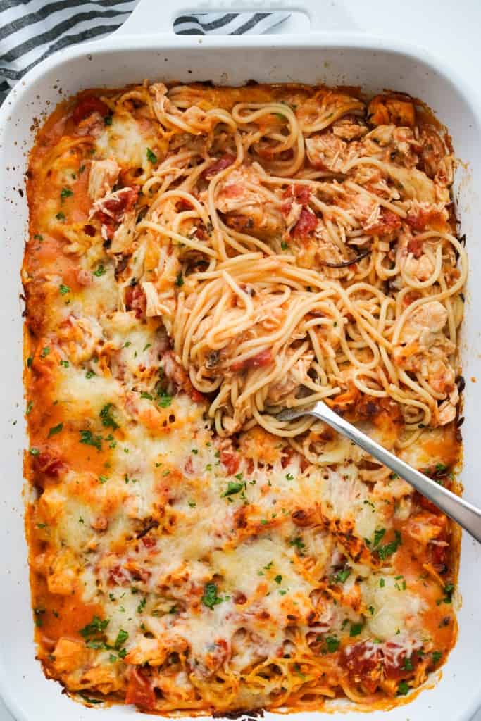 A casserole dish of chicken spaghetti in red tomato sauce, topped with melted cheese