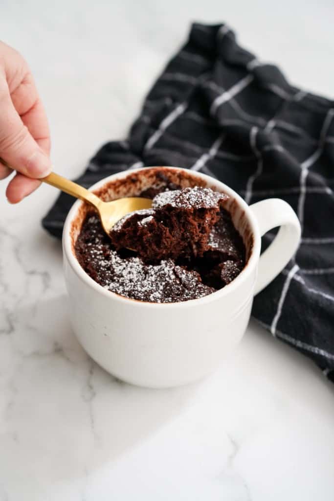 Digging into chocolate mug cake topped with powdered sugar