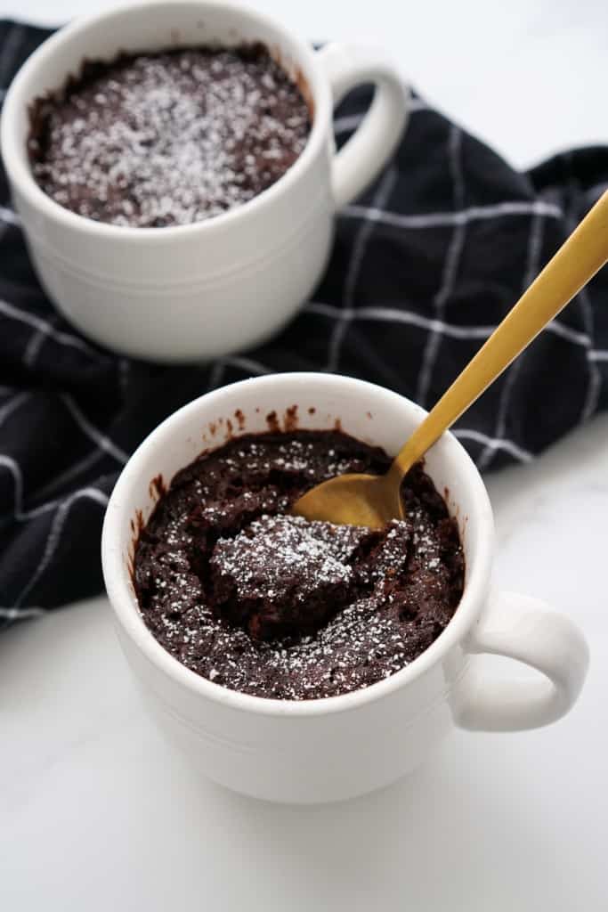 Two chocolate cake made in mugs topped with powdered sugar