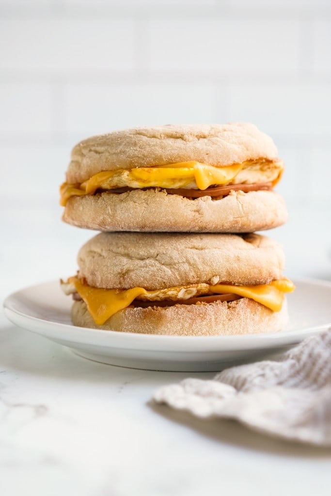Two breakfast sandwich made with english muffin loaded with egg, cheese and canadian bacon on a plate