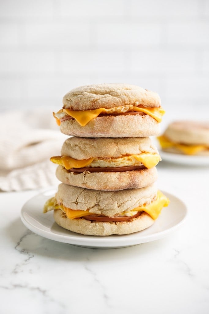 A stack of english muffin breakfast sandwich loaded with fried eggs, cheese and canadian bacon