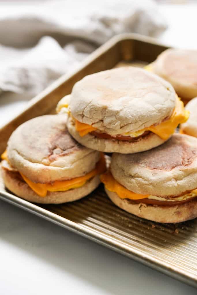 A bunch of english muffin breakfast sandwich on a baking sheet