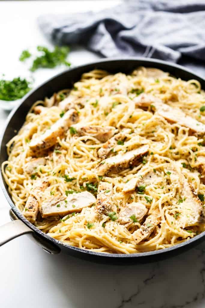 Spaghetti pasta with sliced chicken breast in a large skillet, topped with parmesan and parsley