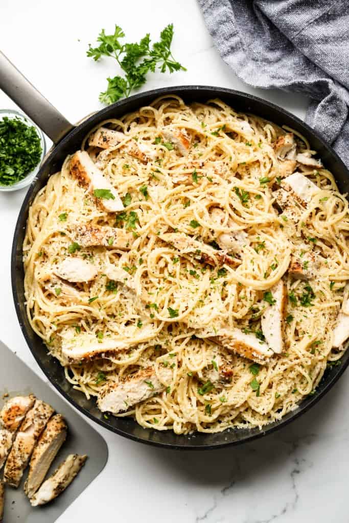 A large skillet loaded with garlic parmesan pasta with chicken strips on top.
