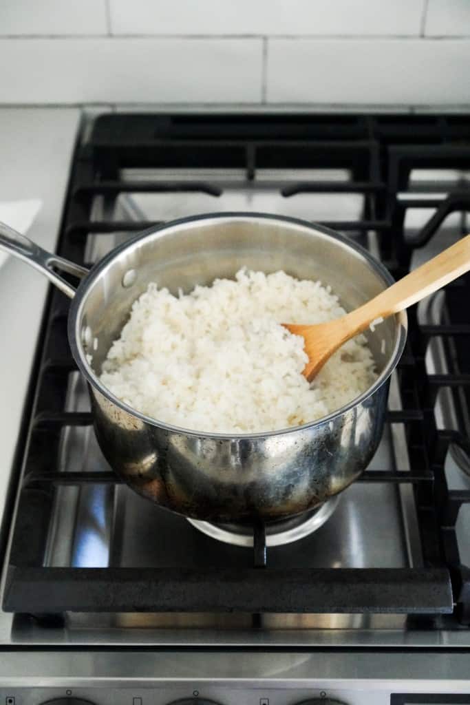 Fluffing sushi rice with a wooden spoon in a pot on stovetop