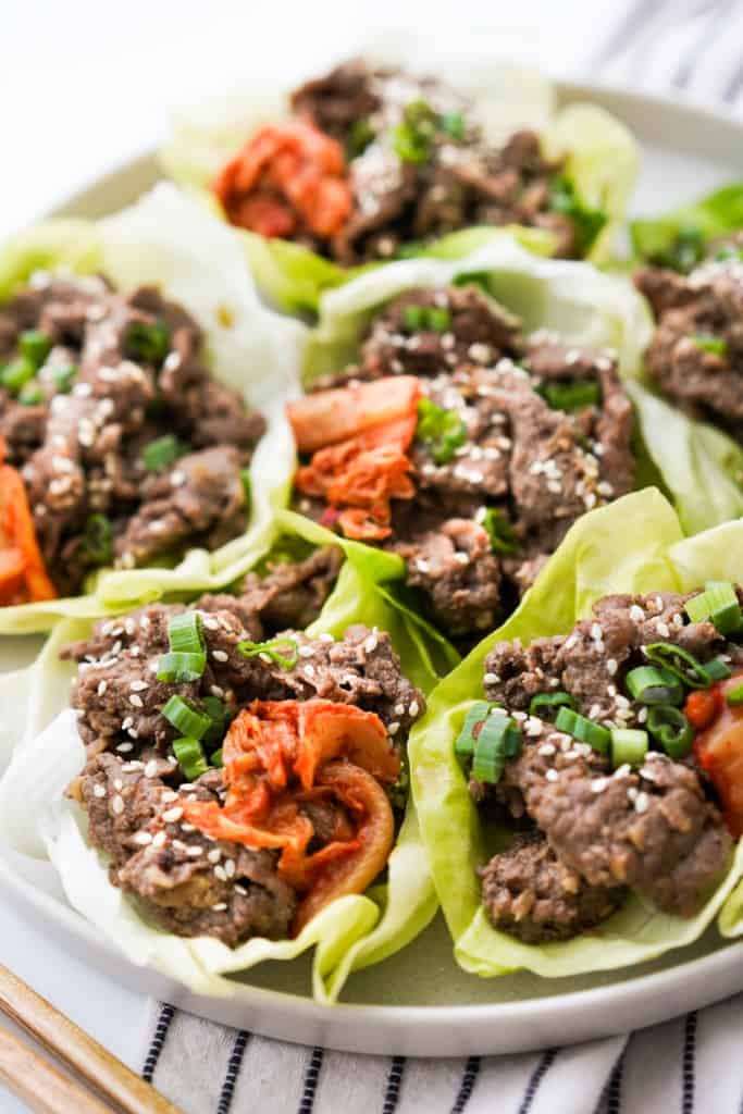 A plate full of korean beef lettuce wraps with kimchi, sesame seeds and green onions on top