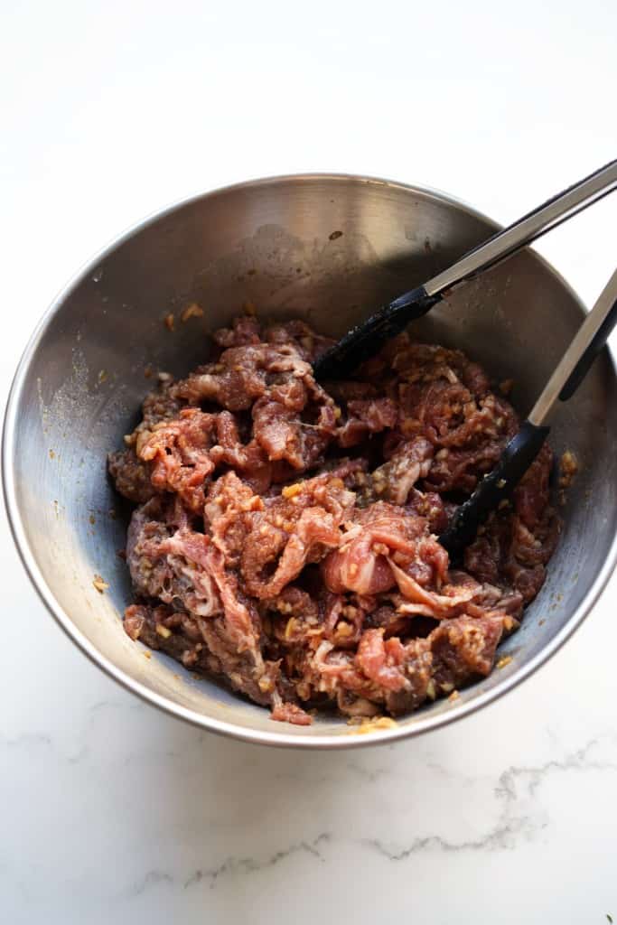 Marinated beef in a metal mixing bowl