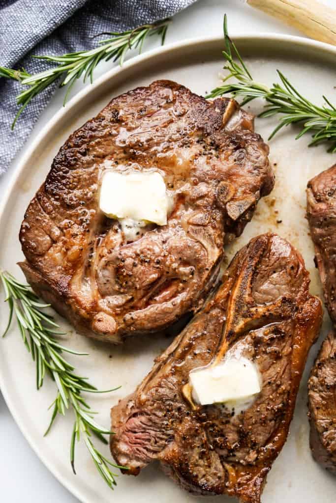 Two pieces of pan seared lamb chops on a plate surrounded with fresh rosemary herbs