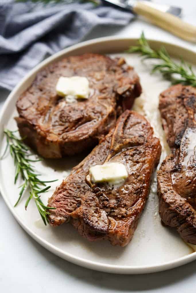 A plate with two pieces of seared lamb chops with rosemary twigs 