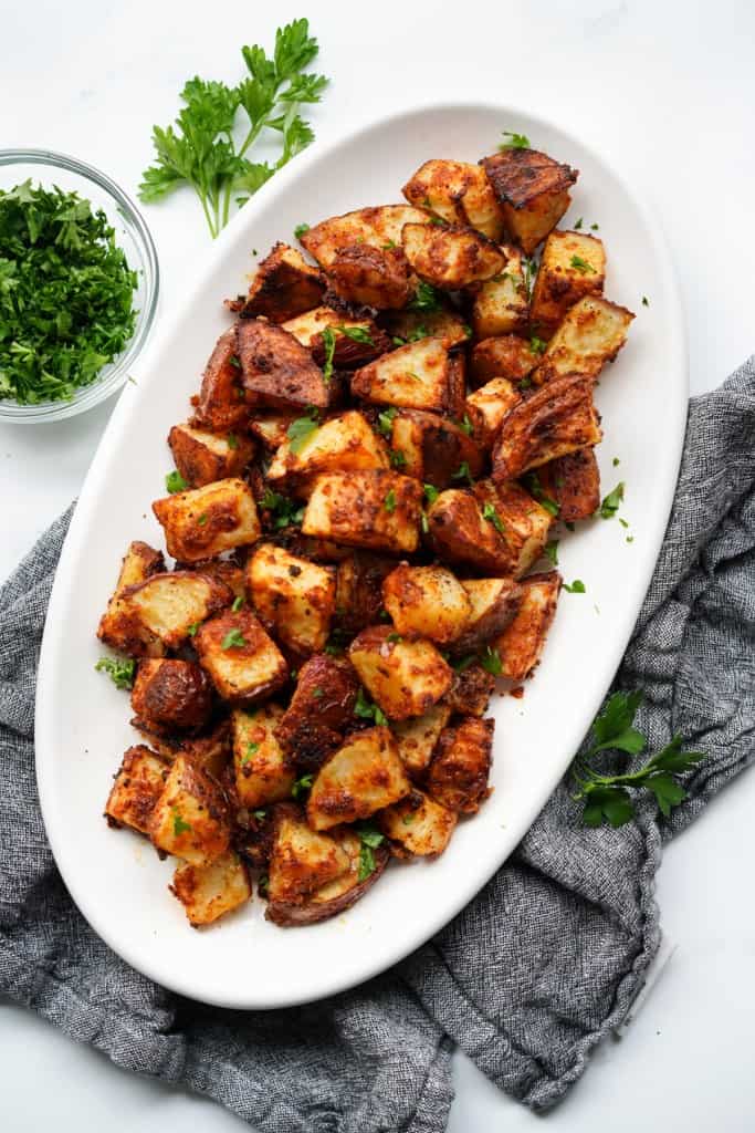 An oval plate of roasted garlic parmesan potatoes in cubes topped with parsley