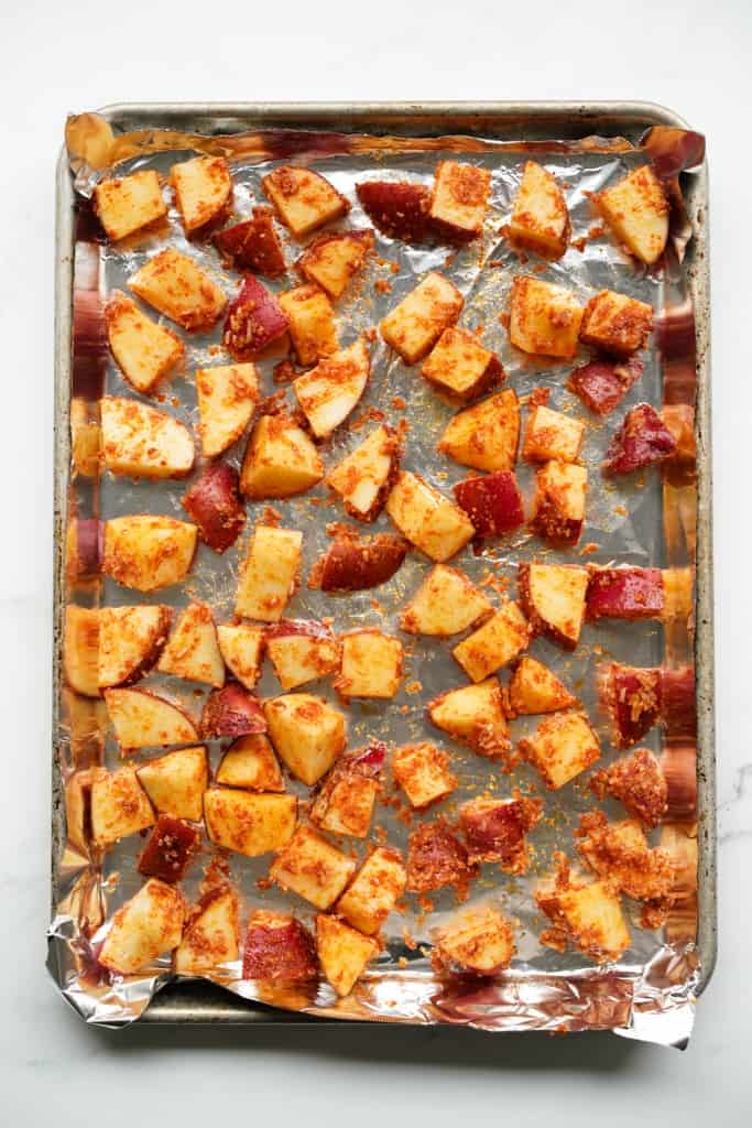 A sheet pan of diced red potatoes coated in paprika, garlic powder and grated parmesan cheese