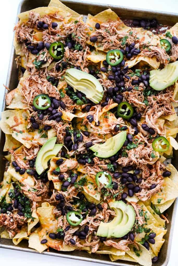Shredded chicken Nachos topped with black beans and avocado slices