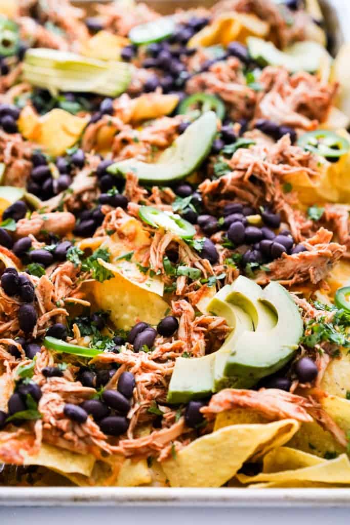 shredded chicken nachos topped with cheese, black beans and avcado