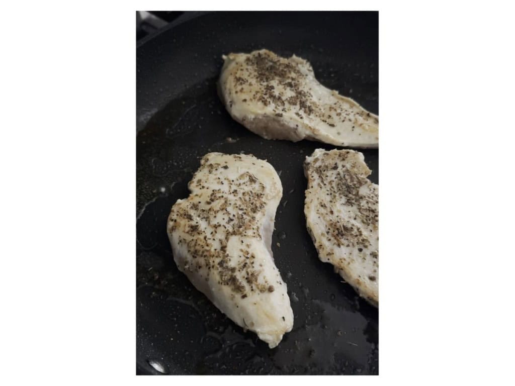 Searing seasoned chicken breast on a skillet