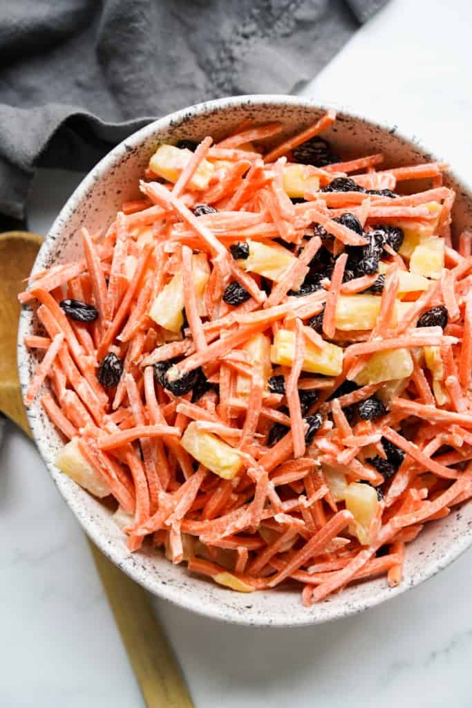Top down view of a bowl of shredded carrots, combined with raisin and pineapple. tossed in creamy sauce