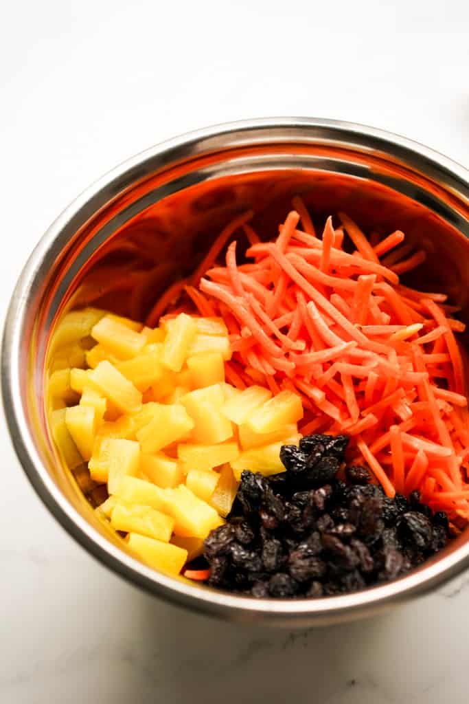 Shredded carrots, pineapple tidbits and raisins in a large mixing bowl