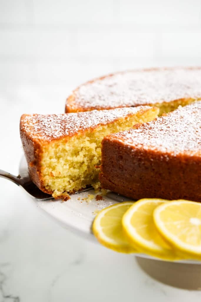 LIfting out a triangular slice of Italian olive oil cake that is sitting on a cake stand.