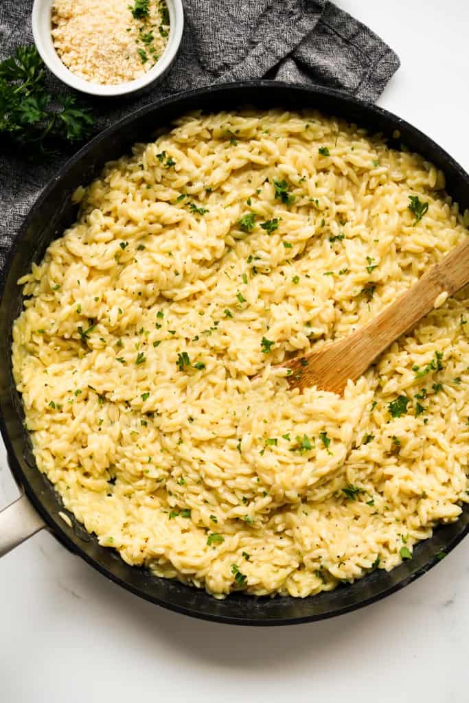 Using a wooden spoon to scoop up creamy parmesan orzo from a skillet
