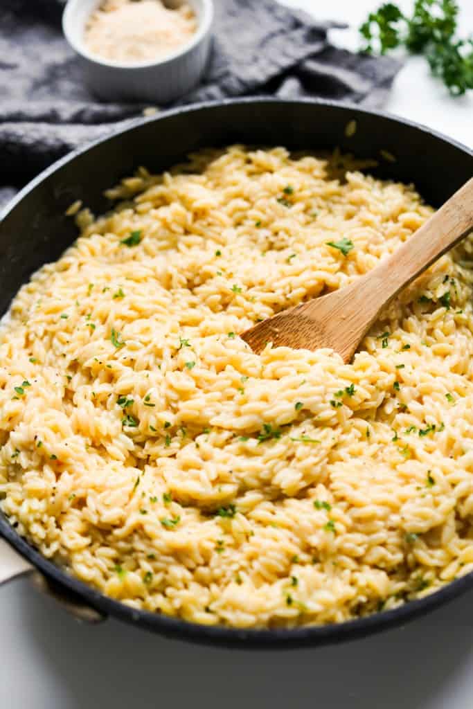 Scooping into a skillet of creamy parmesan orzo