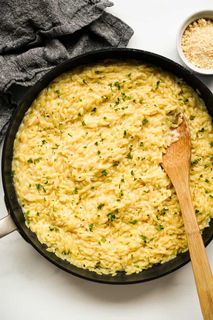 A top down view of creamy orzo with a wooden spoon in the skillet