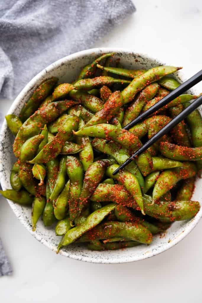 Chopsticks picking up spicy garlic edamame in pods