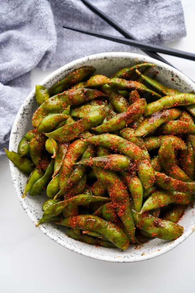 A bowl of edamame coated in hoisin sauce and topped with togarashi spicy powder.