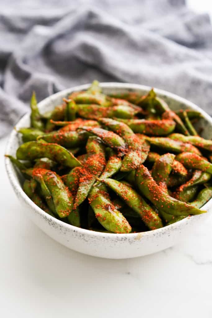 A bowl of edamame coated in hoisin sauce and topped with togarashi