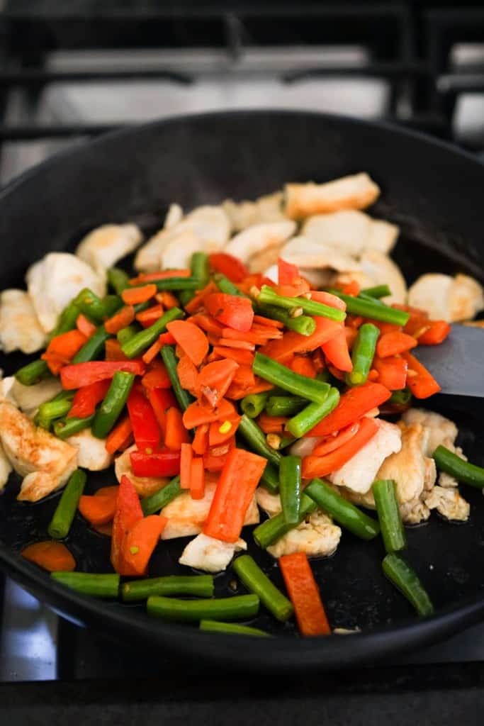 Adding veggies to chicken in skillet