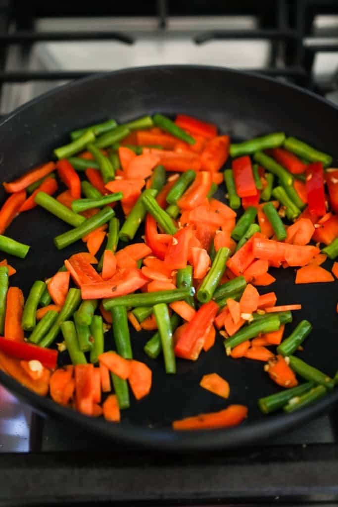 cooking bell peppers, carrots and green beans in a skillet