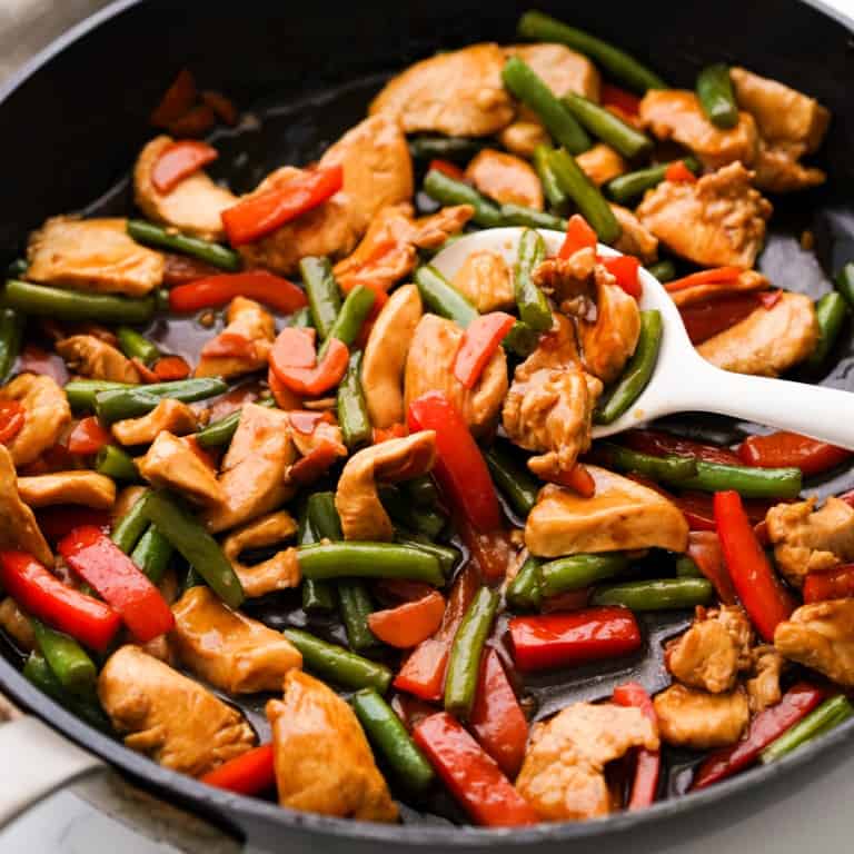 A skillet loaded with chicken pieces, red bell peppers, green beans and carrots, tossed in teriyaki sauce