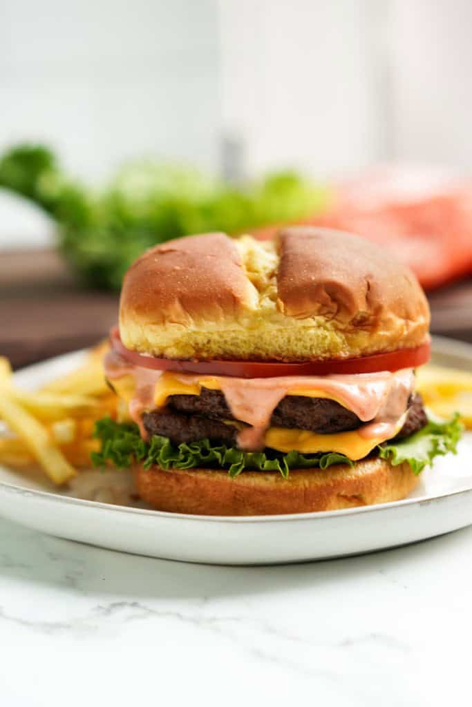 Brioche bun loaded with two meat patties topped with melted cheese, lettuce, tomatoes and sauce.