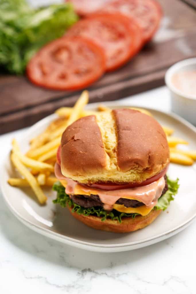 A smash burger loaded with double patties, with fries in the background.