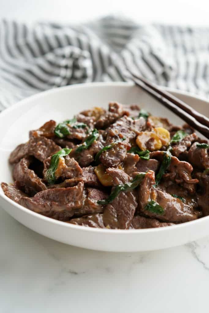 A bowl of stir fry beef tossed with spring onions and sliced ginger