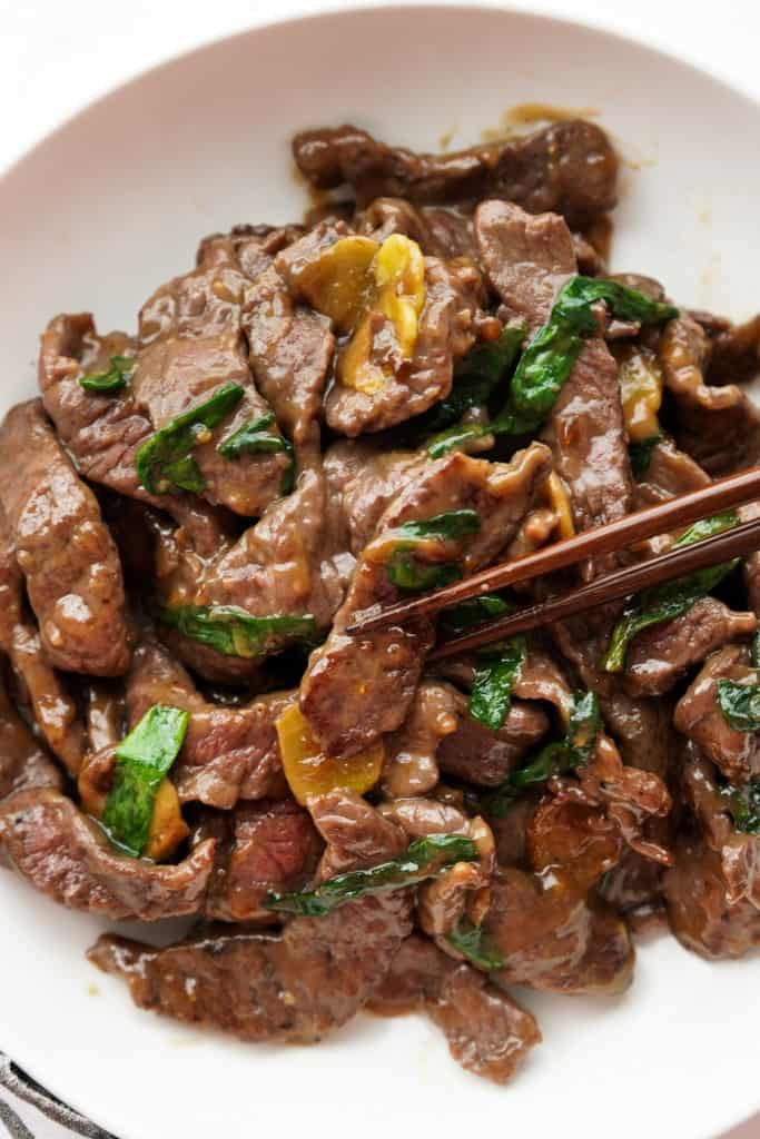 Lifting up a slice of beef from a plate of stir fry beef