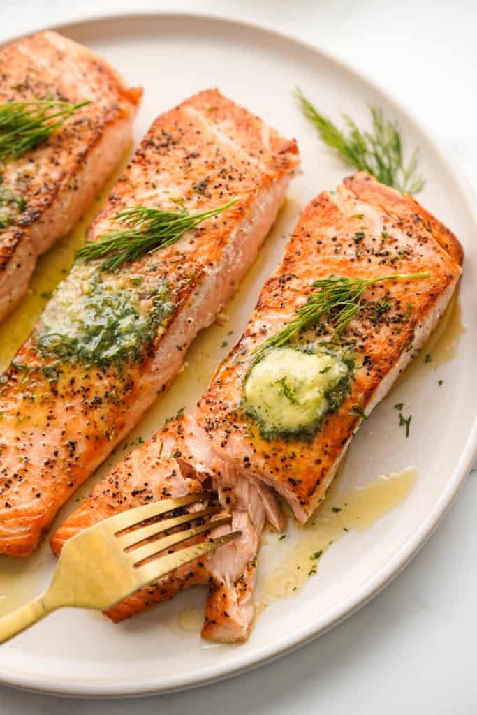 Using a gold fork to cut into a piece of salmon fillet