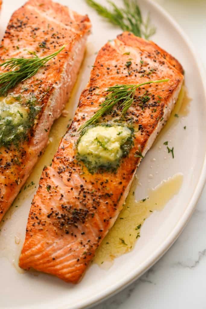 A fillet of seared salmon topped with garlic dill butter compound