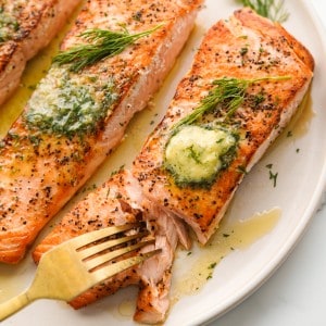 Fork cutting into a piece of salmon topped with garlic dill butter compound