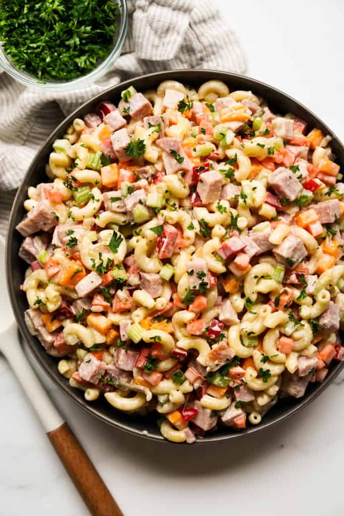 A large bowl of macaroni ham salad combined with bell peppers, celery and carrots