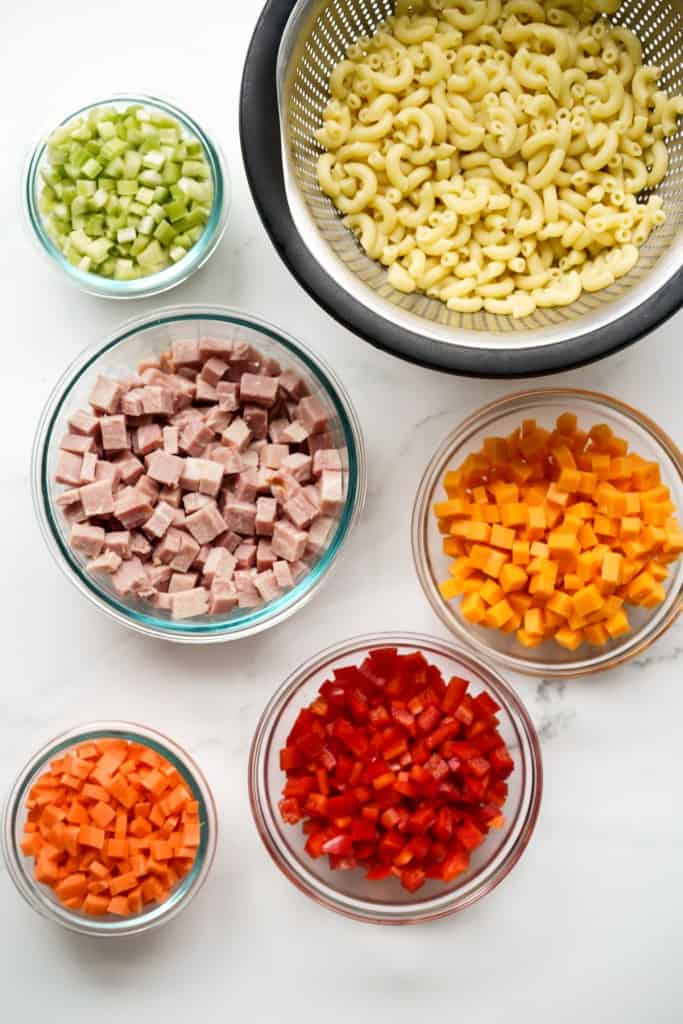 Ingredients in separate bowls: macaroni, celery, ham, carrots, bell peppers