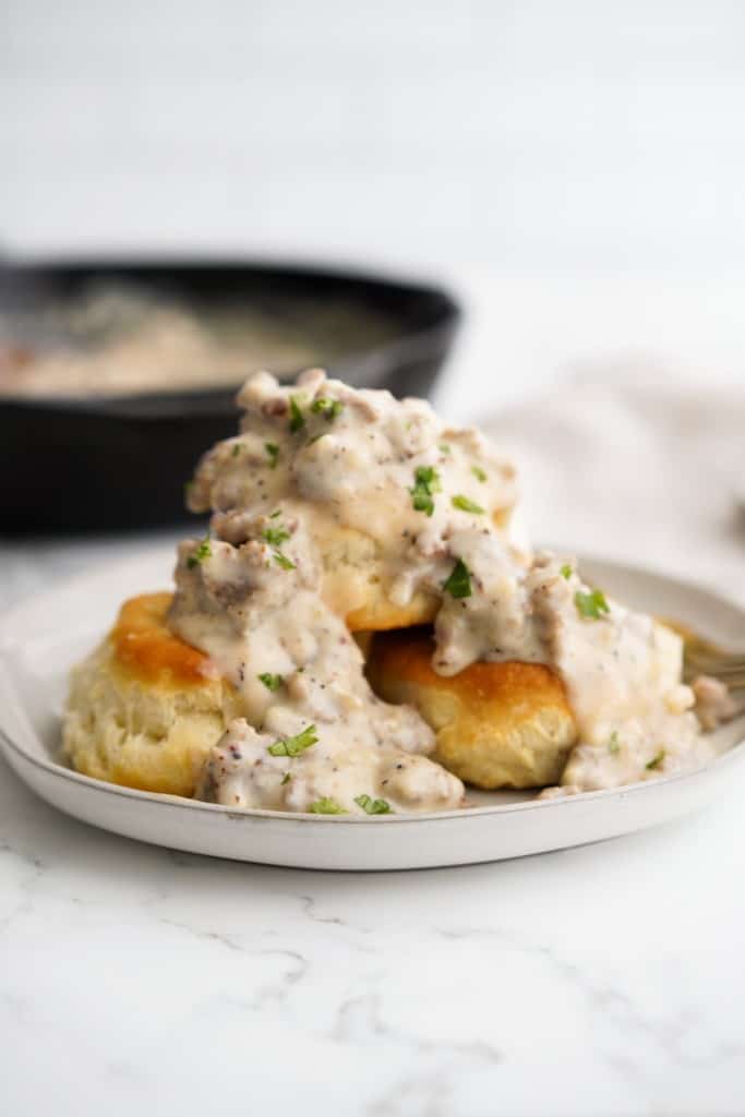 Southern sausage gravy smothered over a stack of biscuits on a plate