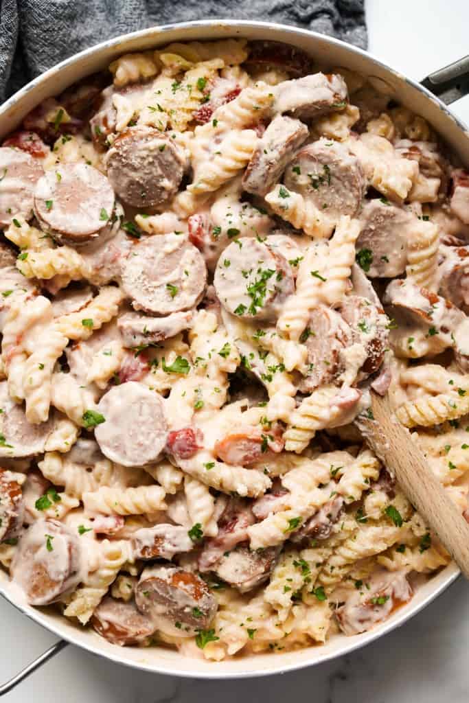 A large skillet loaded with creamy smoked sausage pasta with tomatoes, topped with fresh parsley