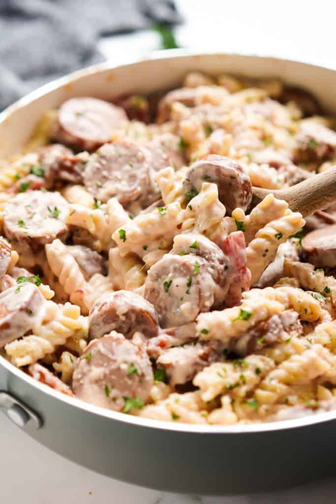 Scooping up some creamy pasta and smoked sausage slices with a wooden spoon