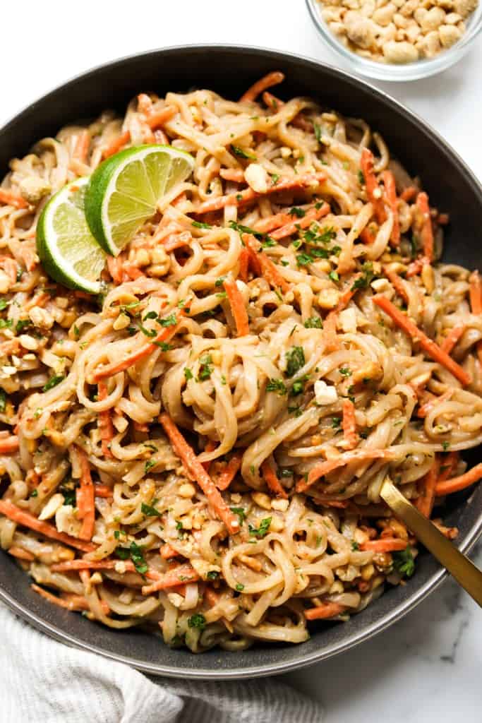 A bowl of rice noodles tossed in sticky peanut sauce, topped with carrots, peanut and cilantro.