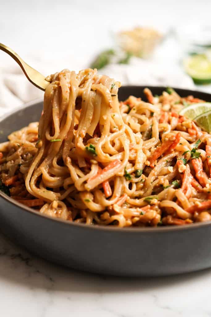 Lifting rice noodles in peanut sauce from a bowl with a fork