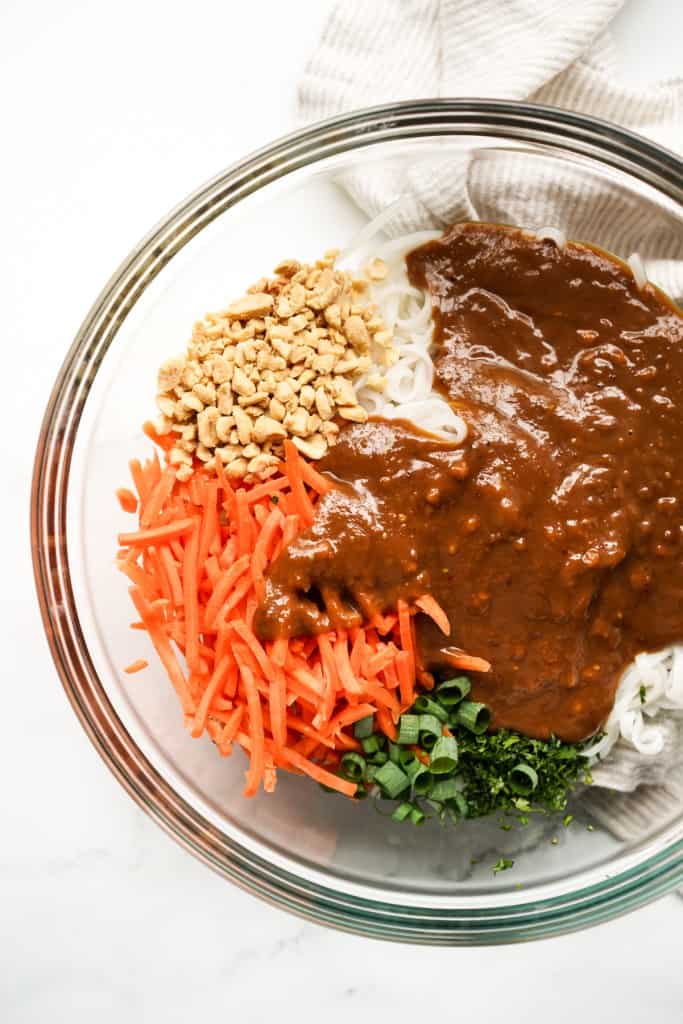 Peanut sauce added to a large bowl of rice noodles, cil;antro, carrots and green onions