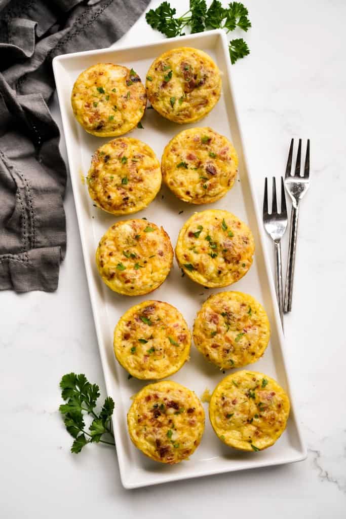 Top down view of cottage cheese bacon egg bites lined up two by two on a rectangular platter 