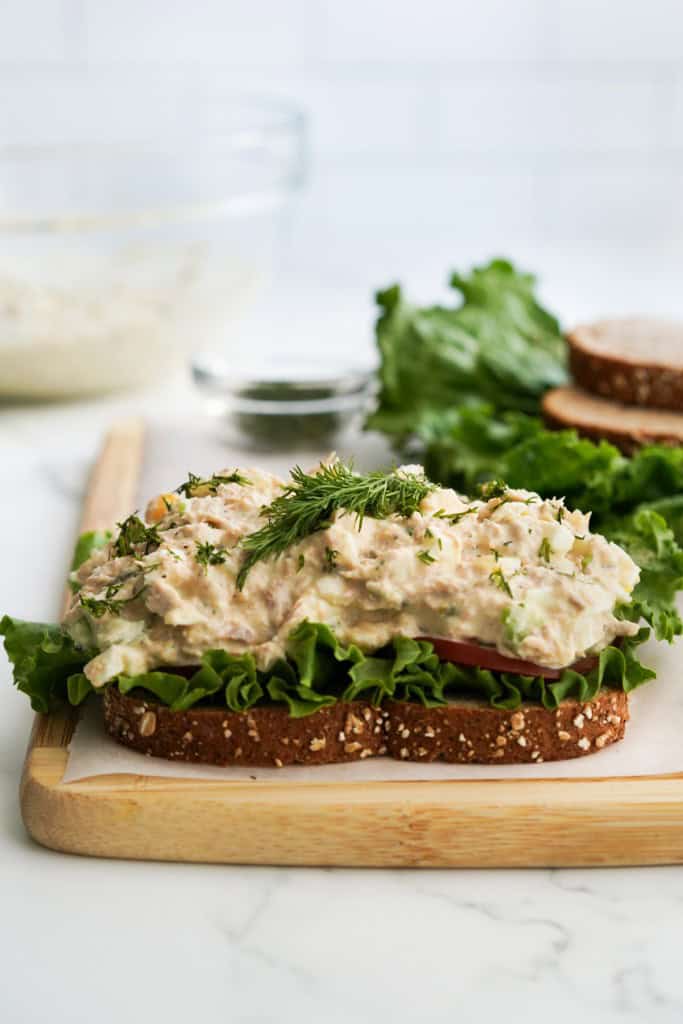 A slice of bread on a wooden cutting board topped with lettuce and tuna egg salad